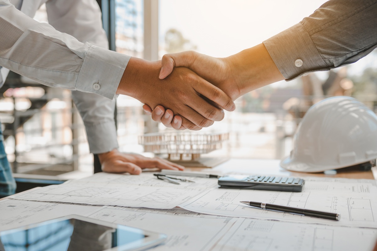 Two people shaking hands over a desk with papers and a white hard hat in Carlsbad.